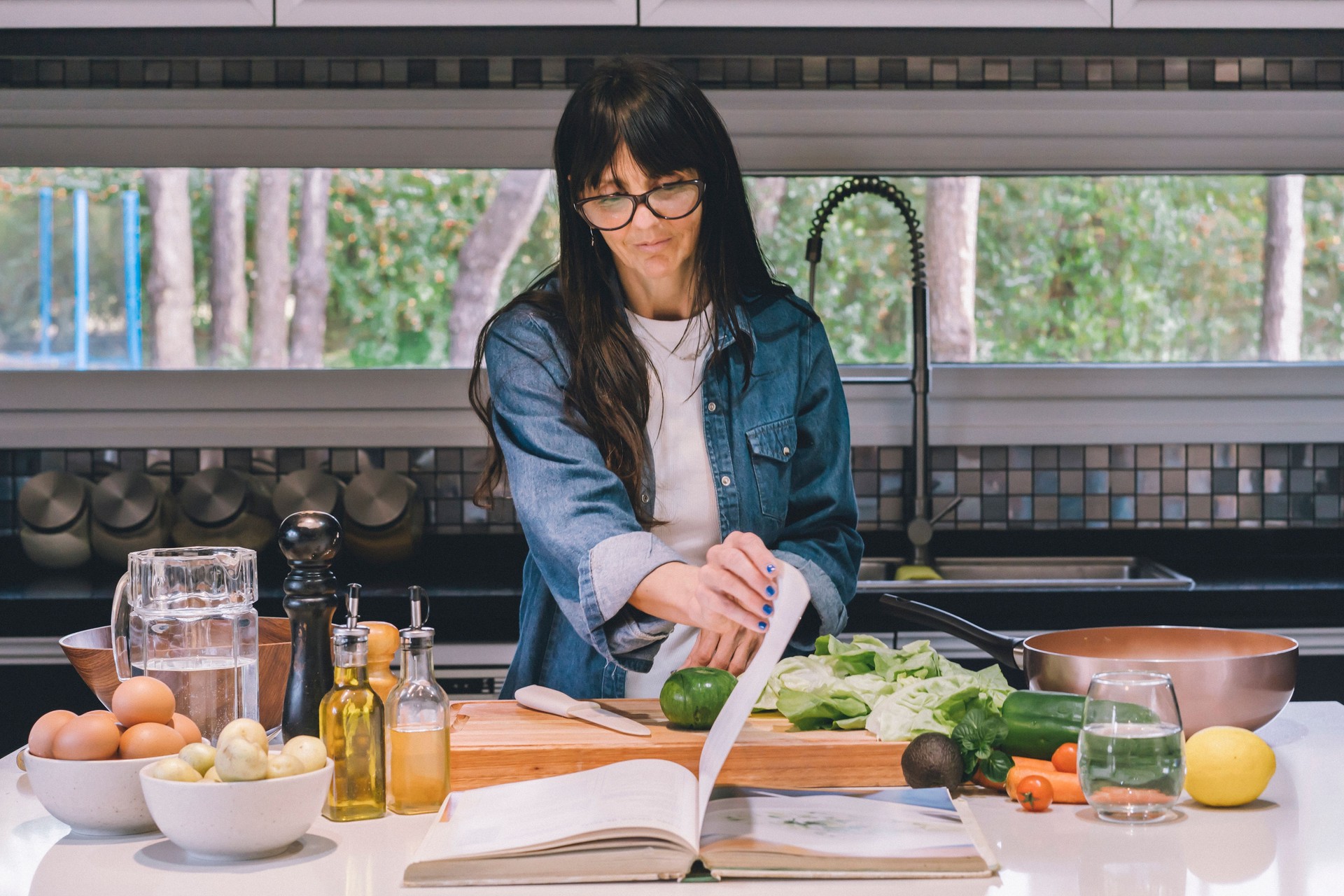 Mid-adult woman reading recipe while preparing food in the kitchen.